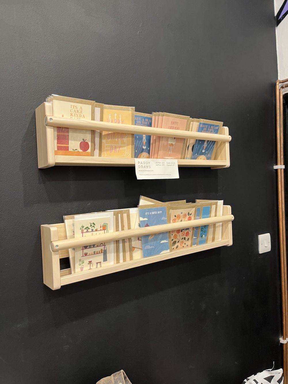 Pale wooden book and zine ledges mounted on a black wall
