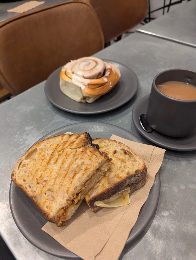 Toasted cheese sandwich, cinnamon bun and coffee on a grey table by a tan leather banquette