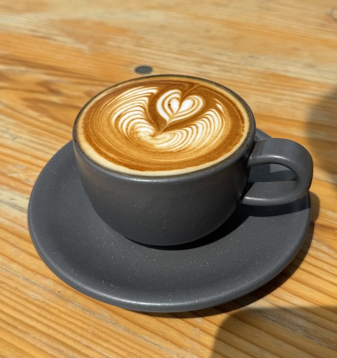 Flat white with rosetta latte art on a pale wooden table