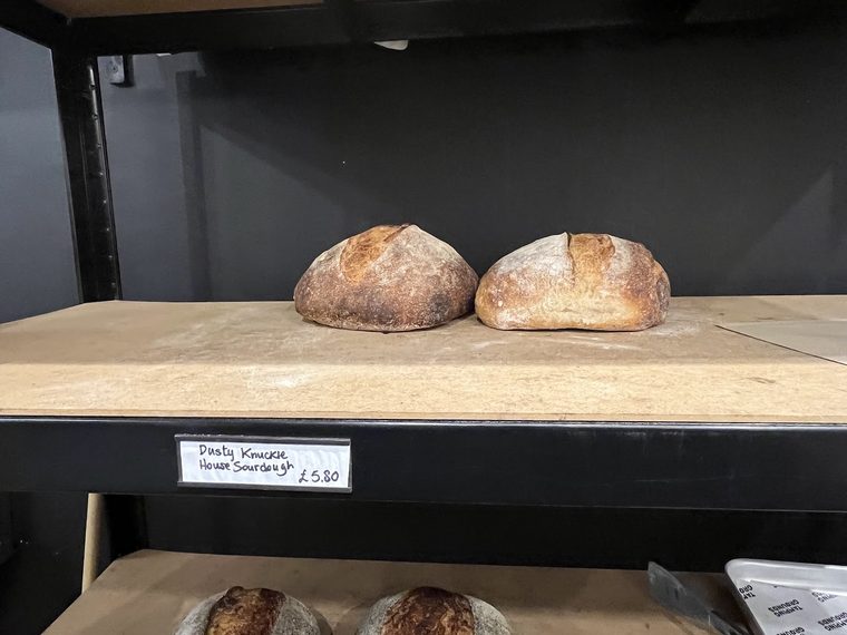 Crusty sourdough loaf on a wooden shelf, cropped away from the price label
