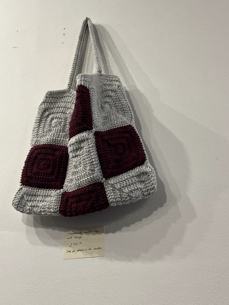 Grey and burgundy crocheted checkerboard tote bag hanging on a white wall